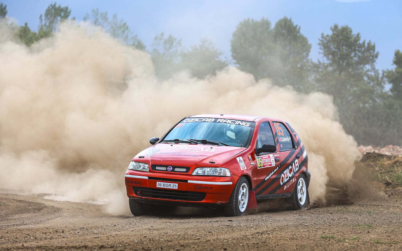 A red car driving through a dirt field